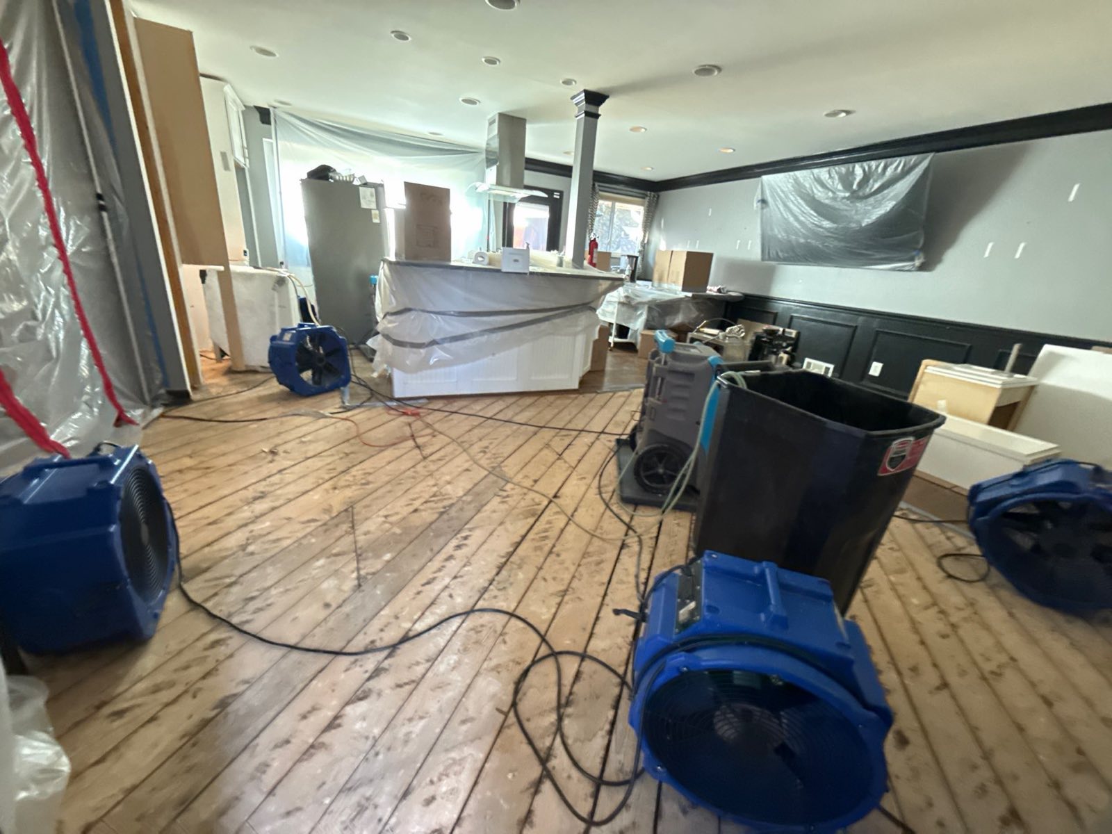 Commercial air movers and drying equipment staged across a water-damaged hardwood floor